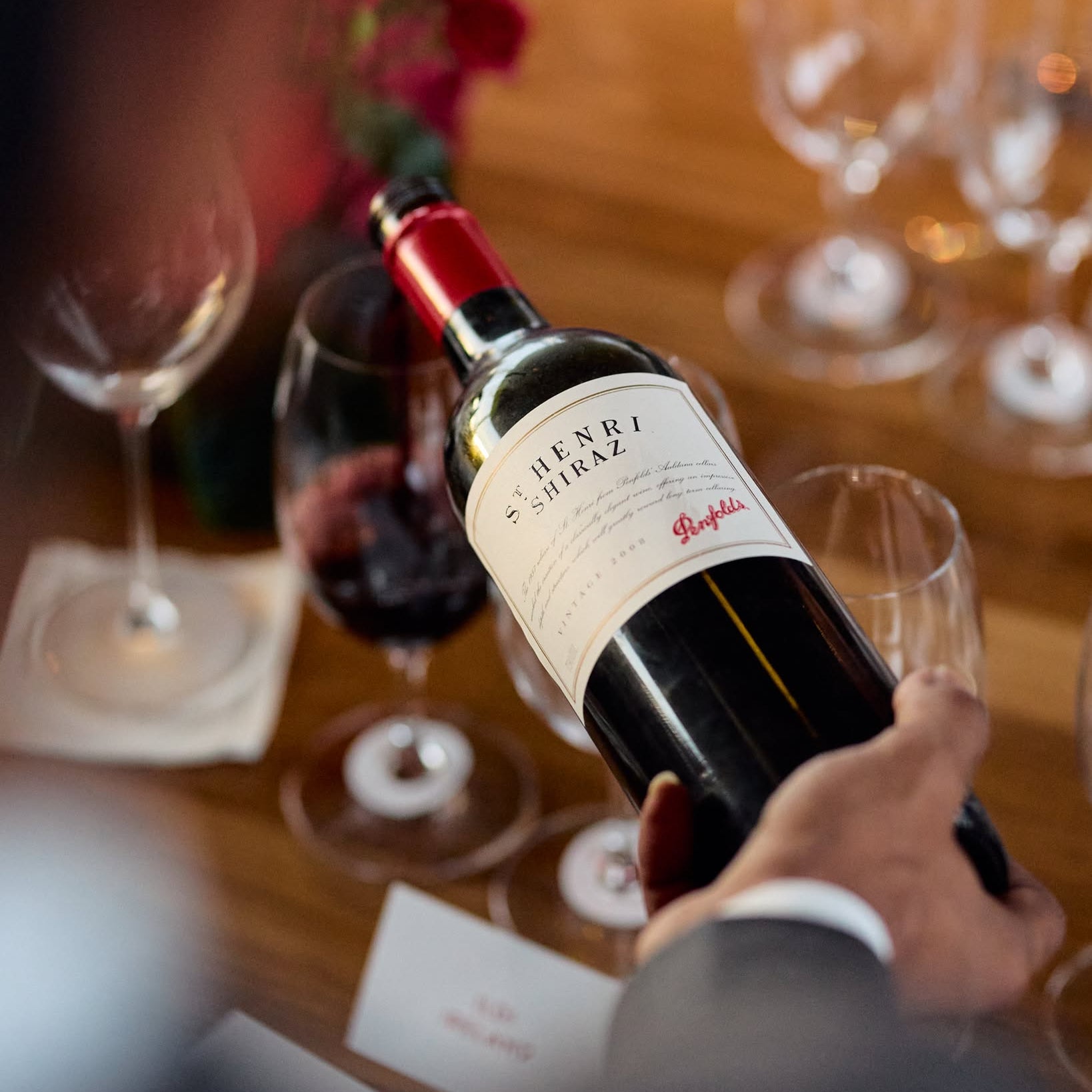 Load image into Gallery viewer, Person holding a bottle of Penfolds St Henri shiraz red wine with glasses on a table
