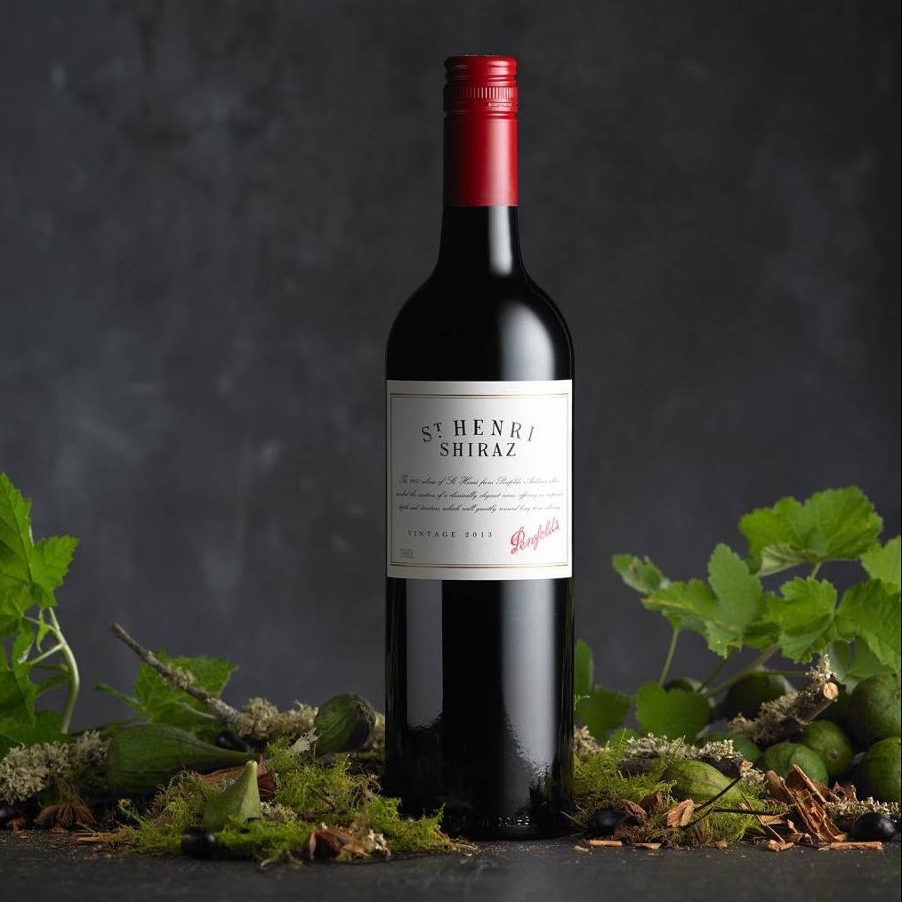 Load image into Gallery viewer, A bottle of St. Henry Shiraz red wine by Penfolds, styled on a dark textured surface with green leaves and moss.
