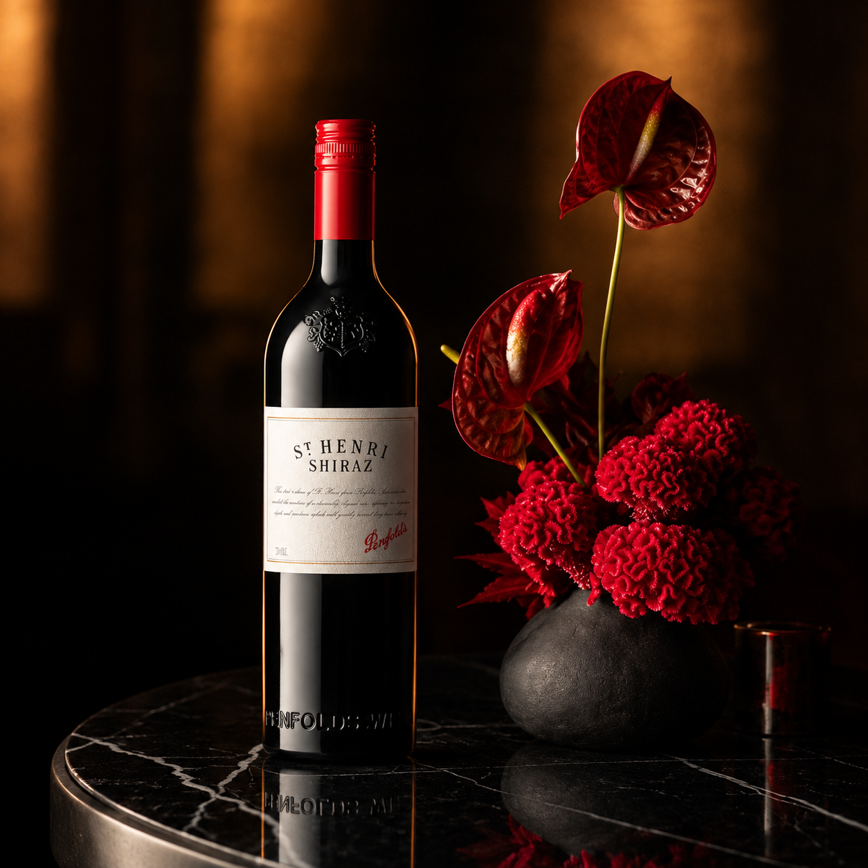 Load image into Gallery viewer, A bottle of Penfolds St. Henri Shiraz red wine stands on a dark marble table beside a black vase filled with red flowers, set against a warm, dark background.