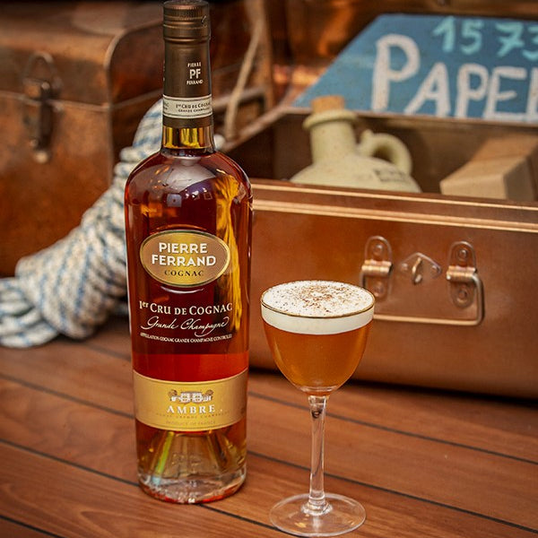 Bottle of Pierre Ferrand Cognac with a glass of cocktail on a wooden surface.