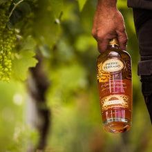 Load image into Gallery viewer, Hand holding a bottle of Pierre Ferrand Cognac with grapes in the background