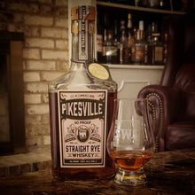 Load image into Gallery viewer, A bottle of Pikesville Whiskey standing on a dark marble table with a tumbler full of whiskey beside it.