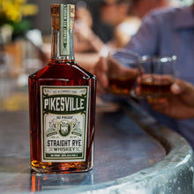 Load image into Gallery viewer, A bottle of Pikesville Whiskey standing on a concrete table with two men making a cheer in the background