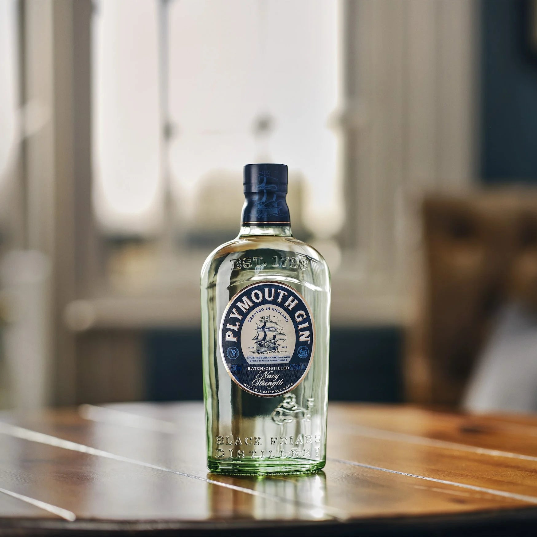 Load image into Gallery viewer, Bottle of Plymouth Navy Strength Gin on a wooden table with a blurred background