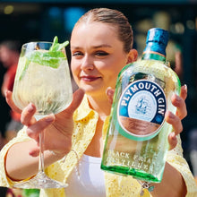 Load image into Gallery viewer, Woman holding a glass of gin and tonic and a bottle of Plymouth Gin.