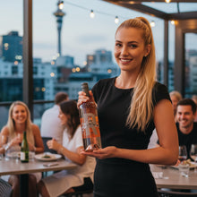 Load image into Gallery viewer, Woman holding a bottle of Poderi Crisci Rose wine in an outdoor evening setting with cityscape in the background