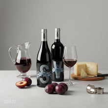 Load image into Gallery viewer, Bottles of Poderi Crisci Syrah and Viburno Red wines next to each other and plums, a cheeseboard, and a wine carafe on a grey surface.