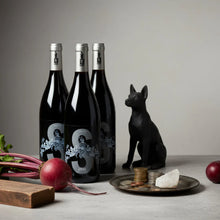 Load image into Gallery viewer, Three wine bottles with a decorative dog figurine and coins on a table.