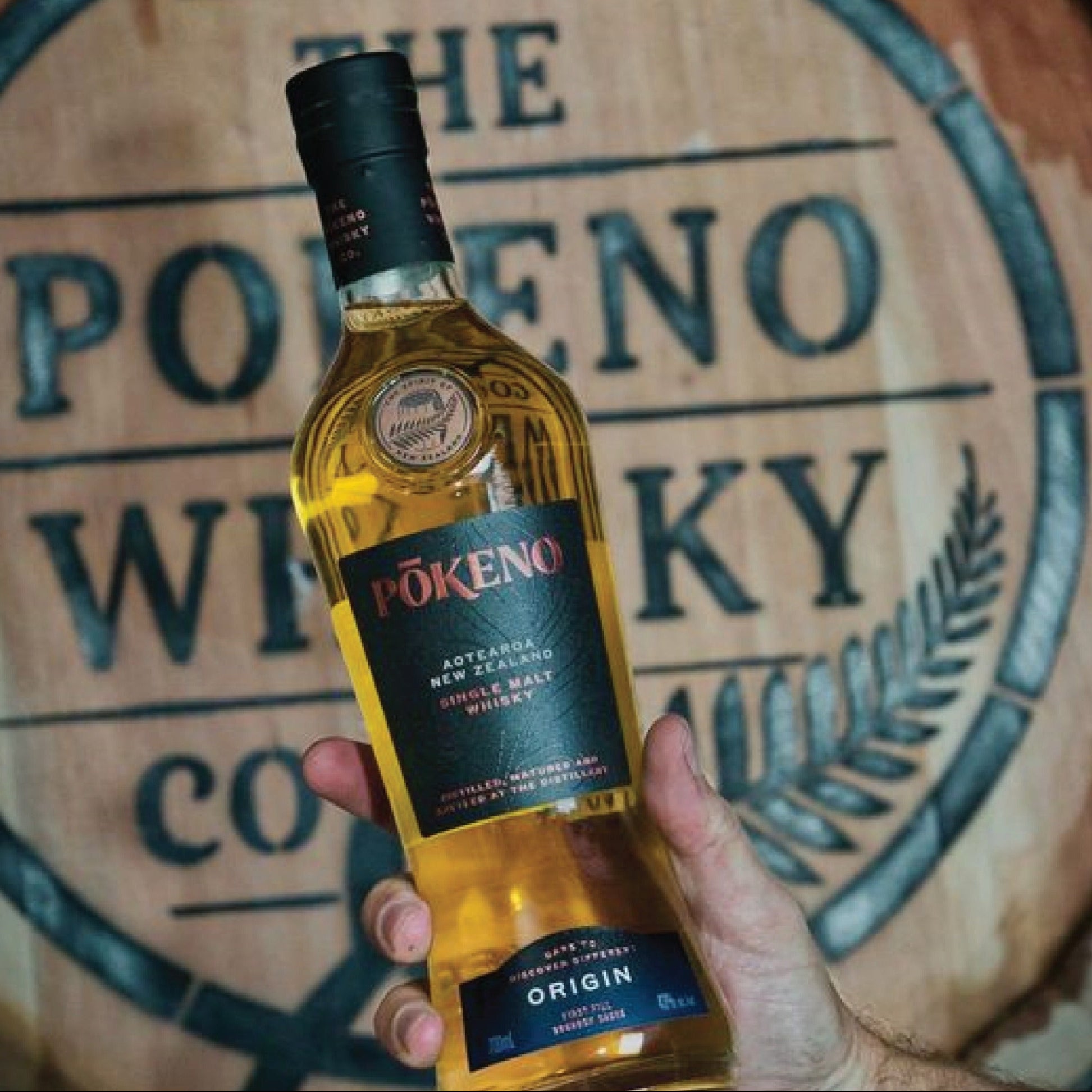 Load image into Gallery viewer, Bottle of Pokeno Origin whisky held in front of a wooden barrel with branding.