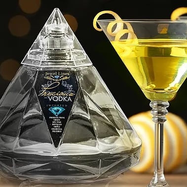 Load image into Gallery viewer, Crystal pyramid-shaped vodka bottle with two cocktails garnished with lemon twists on a blurred background.