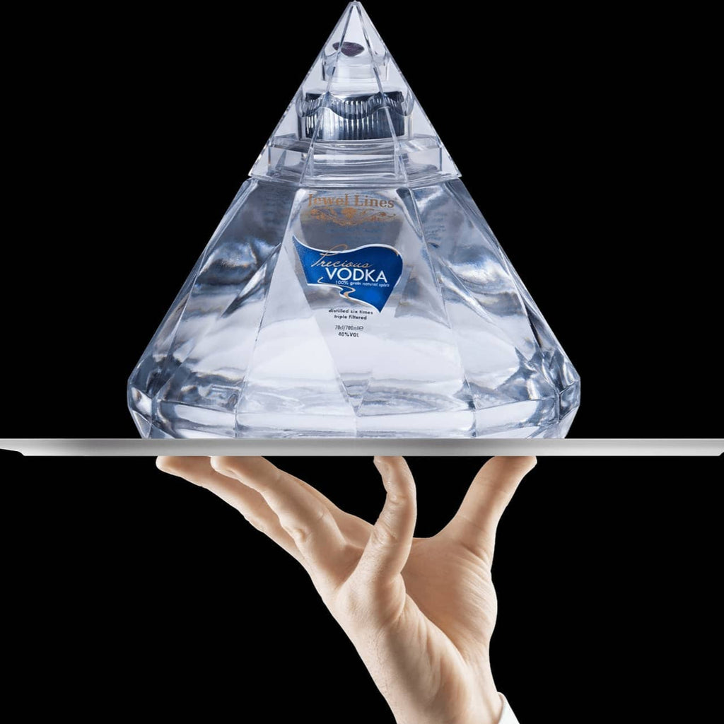 Precious Vodka clear diamond shaped bottle held by a hand on a black background
