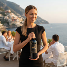 Load image into Gallery viewer, Woman holding a Primitivo di Manduria Riserva Anniversario 62 San Marzano  wine bottle with a scenic background