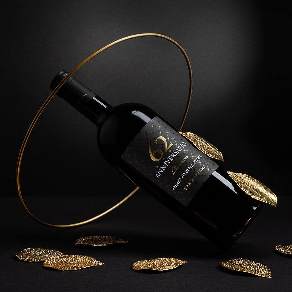Load image into Gallery viewer, A bottle of Primitivo di Manduria Riserva Anniversario 62 San Marzano in a golden decorative metal ring and gold leaves