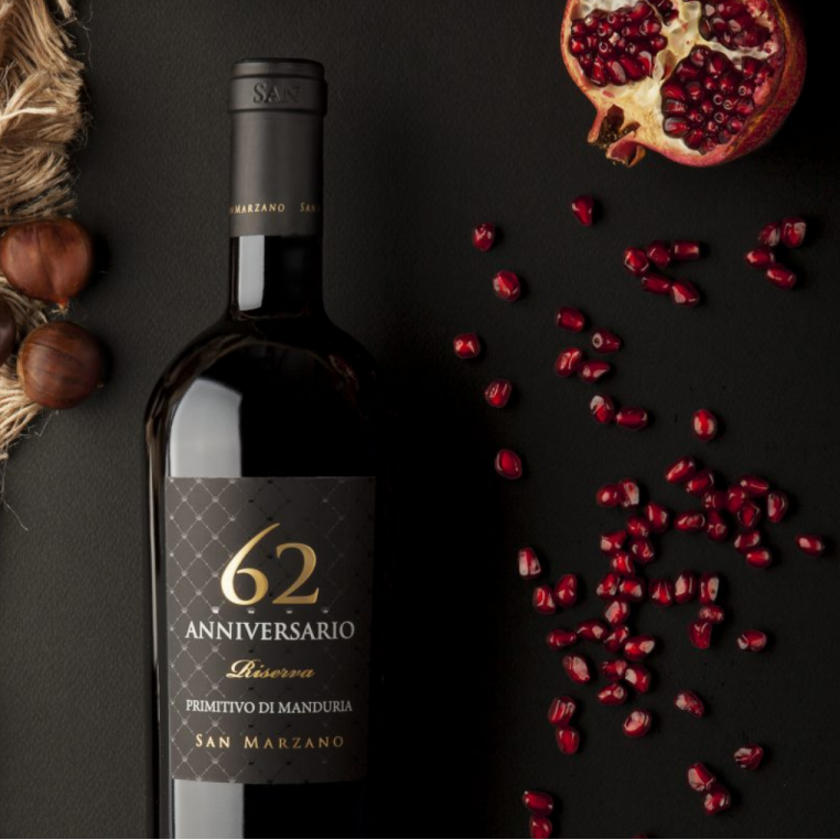 Load image into Gallery viewer, A bottle of Primitivo di Manduria Riserva Anniversario 62 San Marzano next to pomegranate seeds and nuts