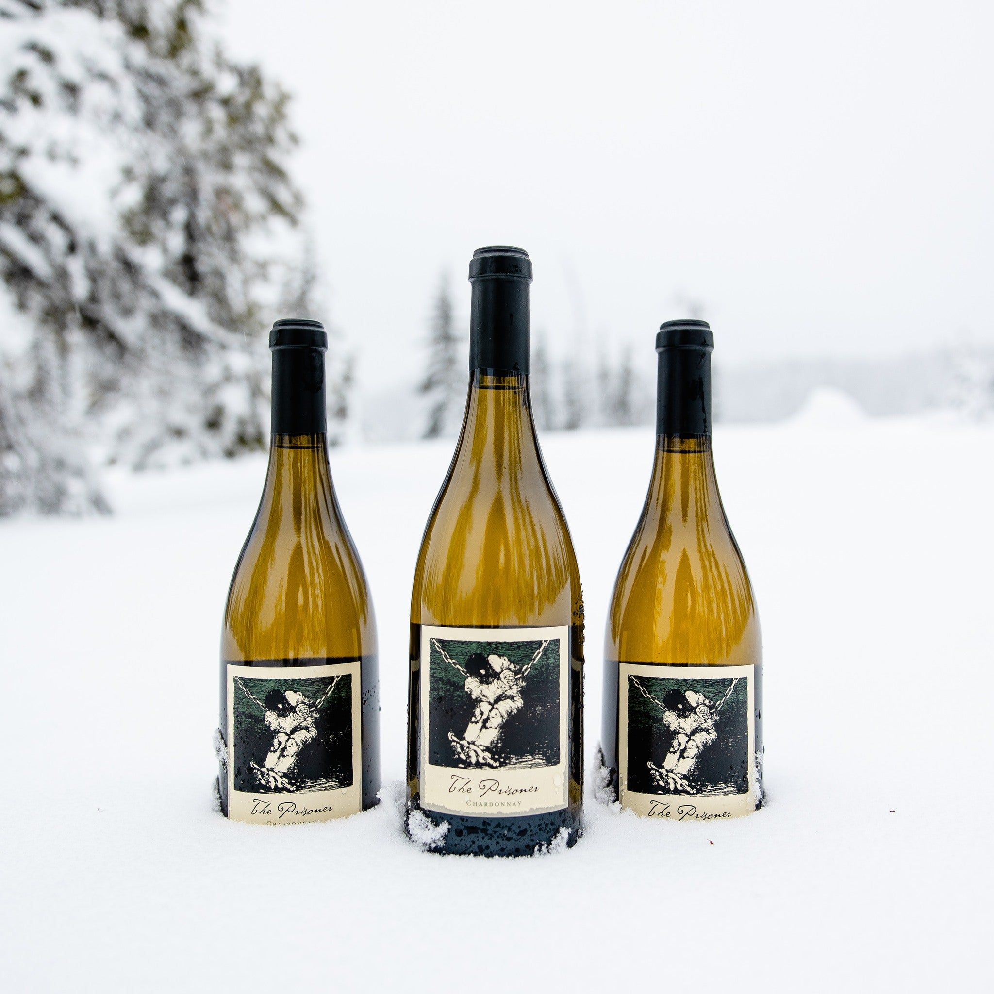 Load image into Gallery viewer, Three bottles of chardonnay standing in snow with a blurry background of pine trees