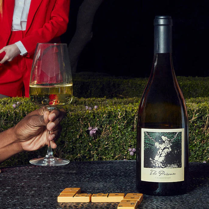 Load image into Gallery viewer, Bottle of wine and glass with a person in a red jacket in the background