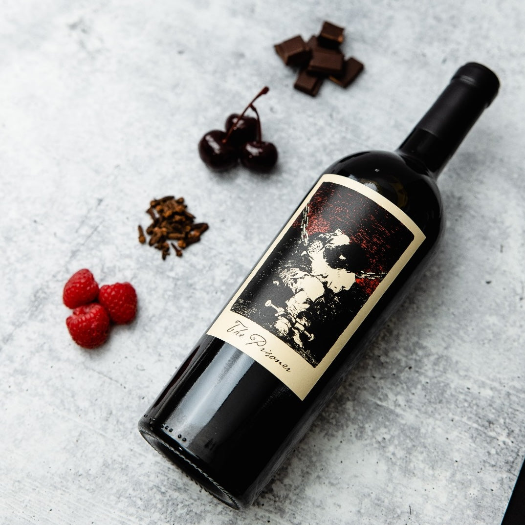 Load image into Gallery viewer, A bottle of The Prisoner Red Blend lying next to berries and chocolates.