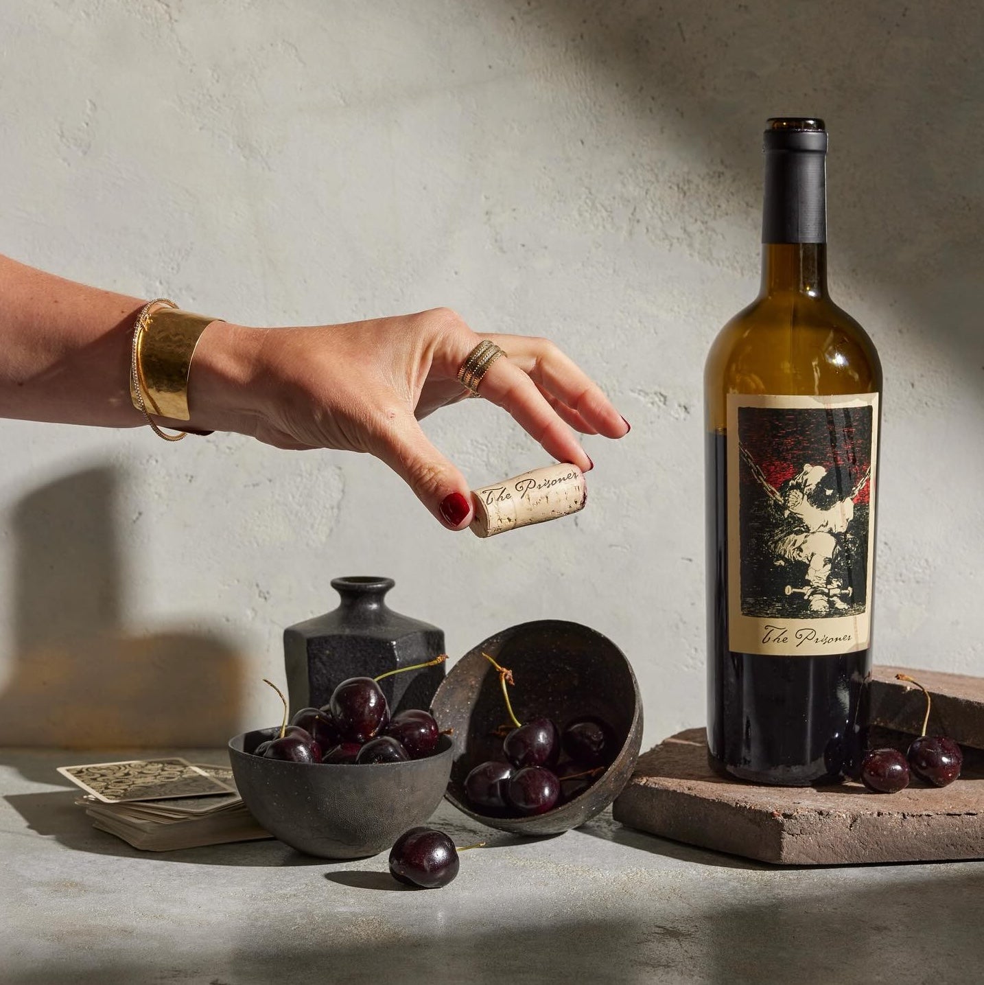 Load image into Gallery viewer, A bottle of The Prisoner Red Blend with two bottles of dark cherries and a women's hand holding a wine cork between her fingers.