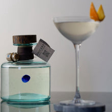 Load image into Gallery viewer, Bottle of Procera Blue Dot-Kenyan Gin with a label and a cocktail in the background
