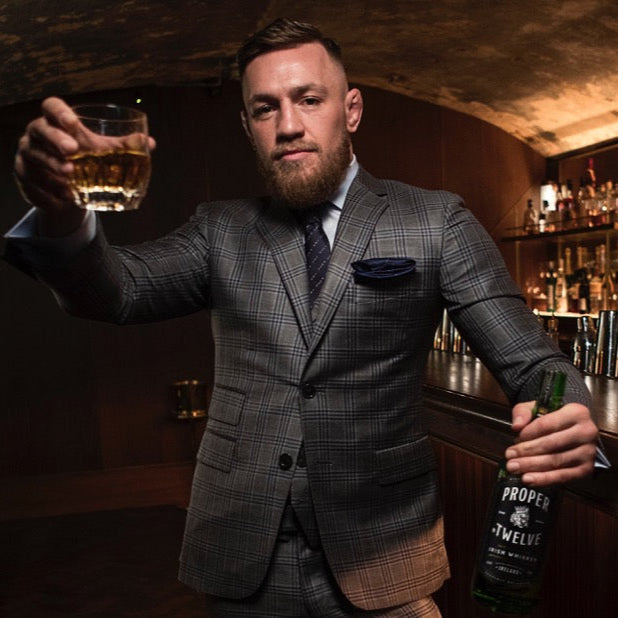 Conor Mcgregor holding a neat glass of whiskey in his hand and the bottle of whiskey in his other hand