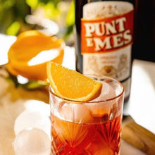 Load image into Gallery viewer, Glass of red cocktail with orange slice and ice cubes, bottle of Punt &amp; Mes in the background.