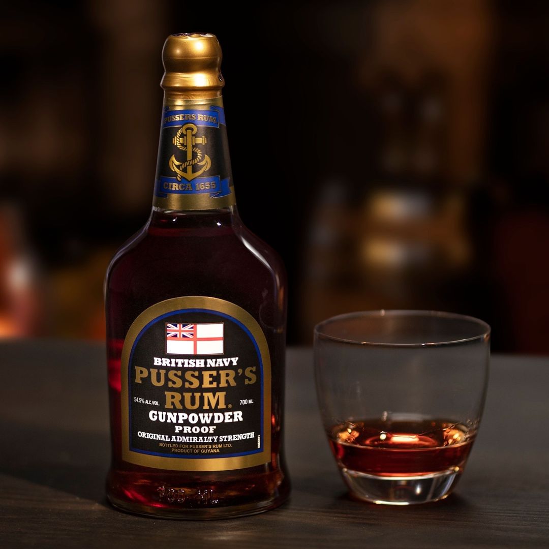 Load image into Gallery viewer, Bottle of Pusser’s Gunpowder Proof Rum with a glass of rum on a dark background