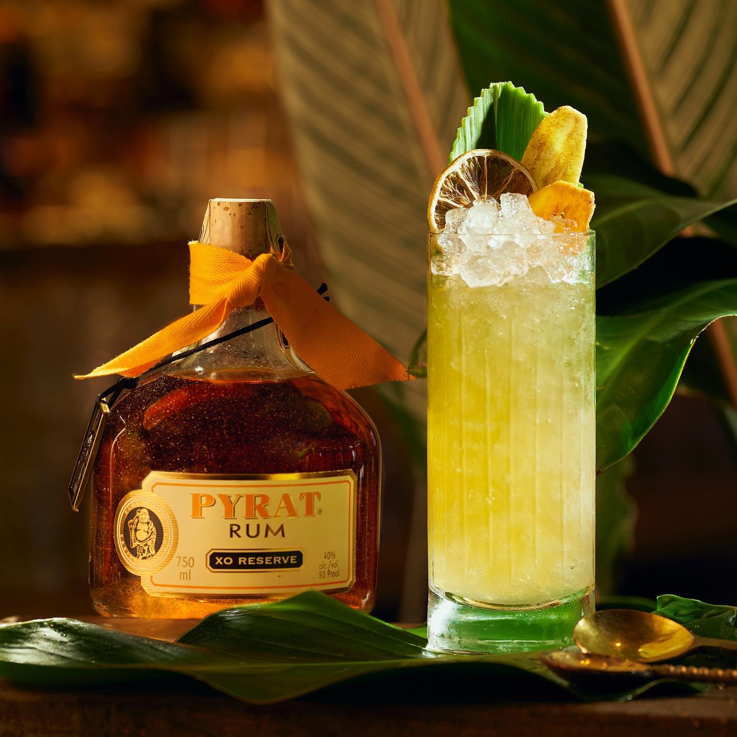 Load image into Gallery viewer, Pyrat XO Reserve Rum bottle with a cocktail garnished with lime and banana on a leafy surface.