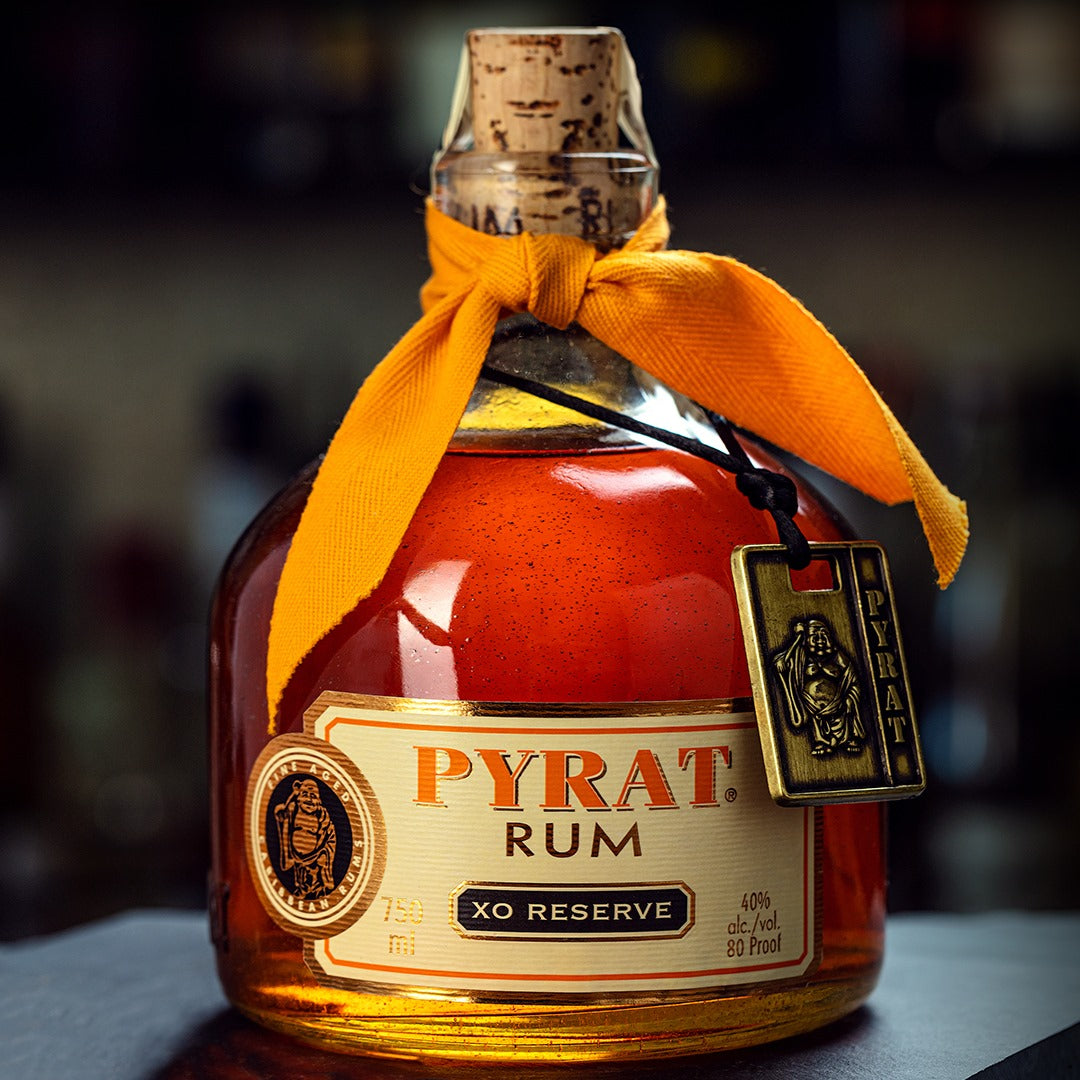 Load image into Gallery viewer, Pyrat XO Reserve Rum bottle with a yellow ribbon and decorative tag on a blurred background