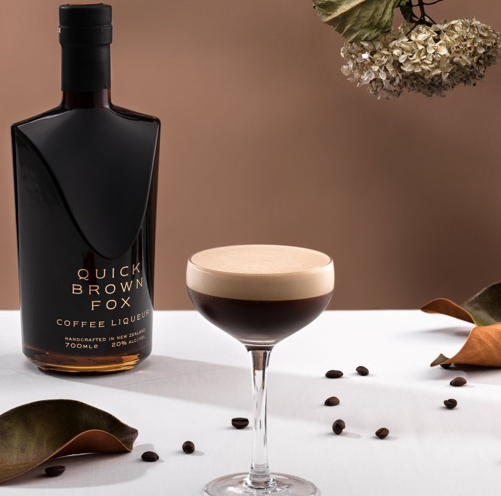 Load image into Gallery viewer, A bottle of Quick Brown Fox Coffee Liqueur with a espresso martini beside it on a white table with some coffee beans spread around the table