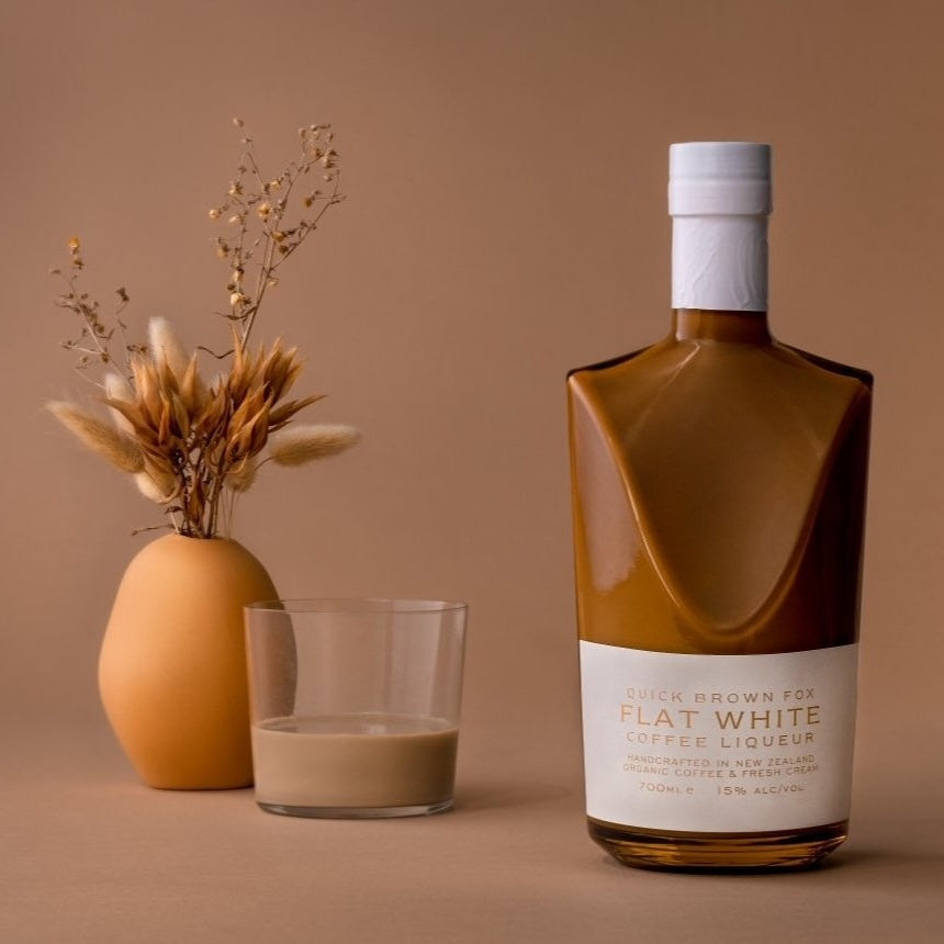Load image into Gallery viewer, A bottle of Quick Brown Fox 'Flat White' Coffee Liqueur and a coffee drink and some dried flowers in vase with a light brown background
