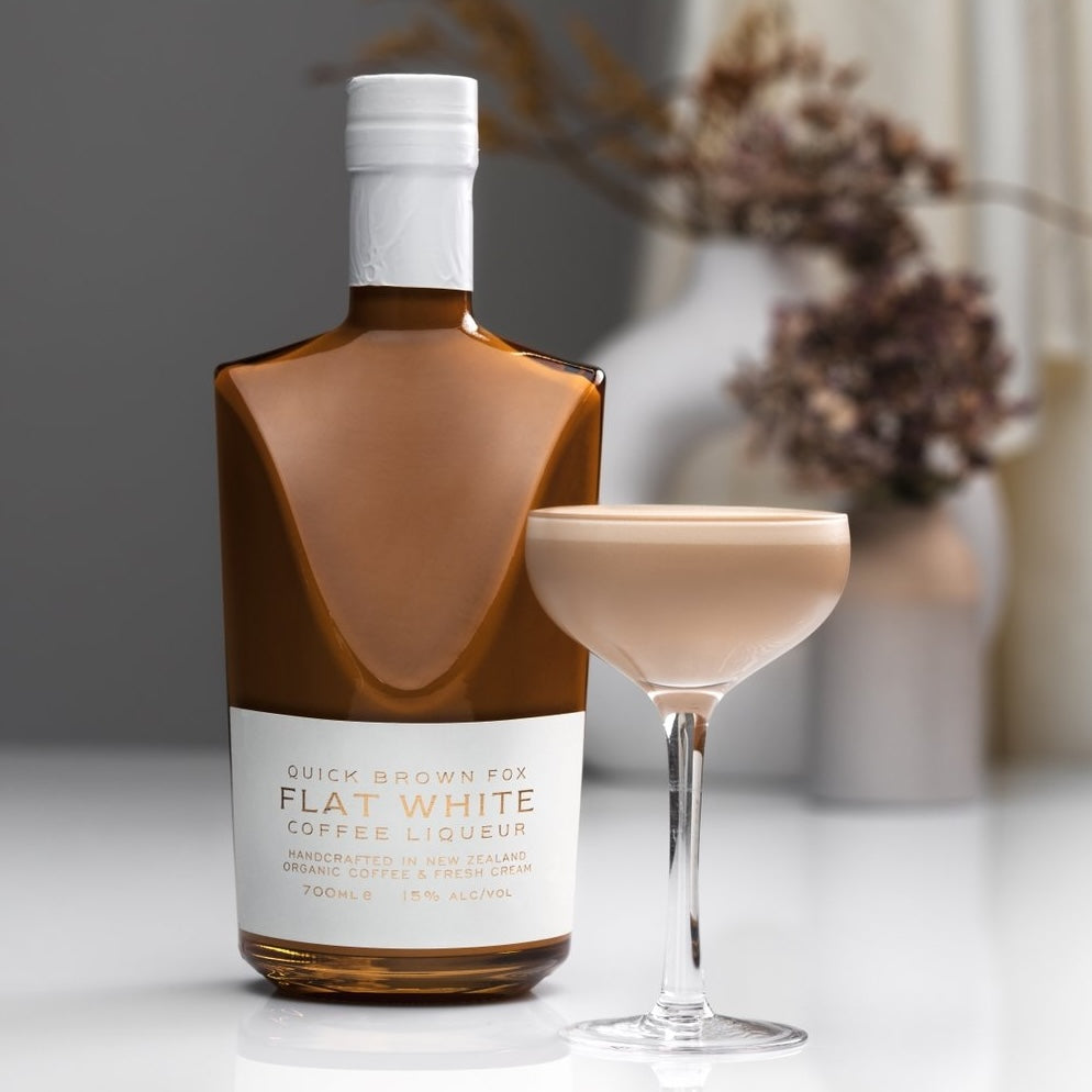 Load image into Gallery viewer, A bottle of Quick Brown Fox 'Flat White' Coffee Liqueur and a coffee cocktail on a white table with a blurry background with some dried flowers