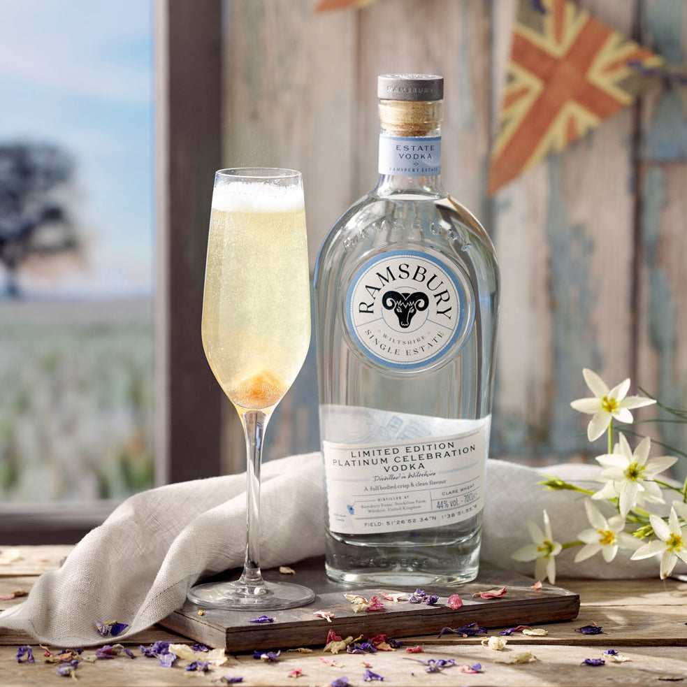 Load image into Gallery viewer, Bottle of Ramsbury vodka with a cocktail in a champagne flute glass on a wooden table with a scenic background.