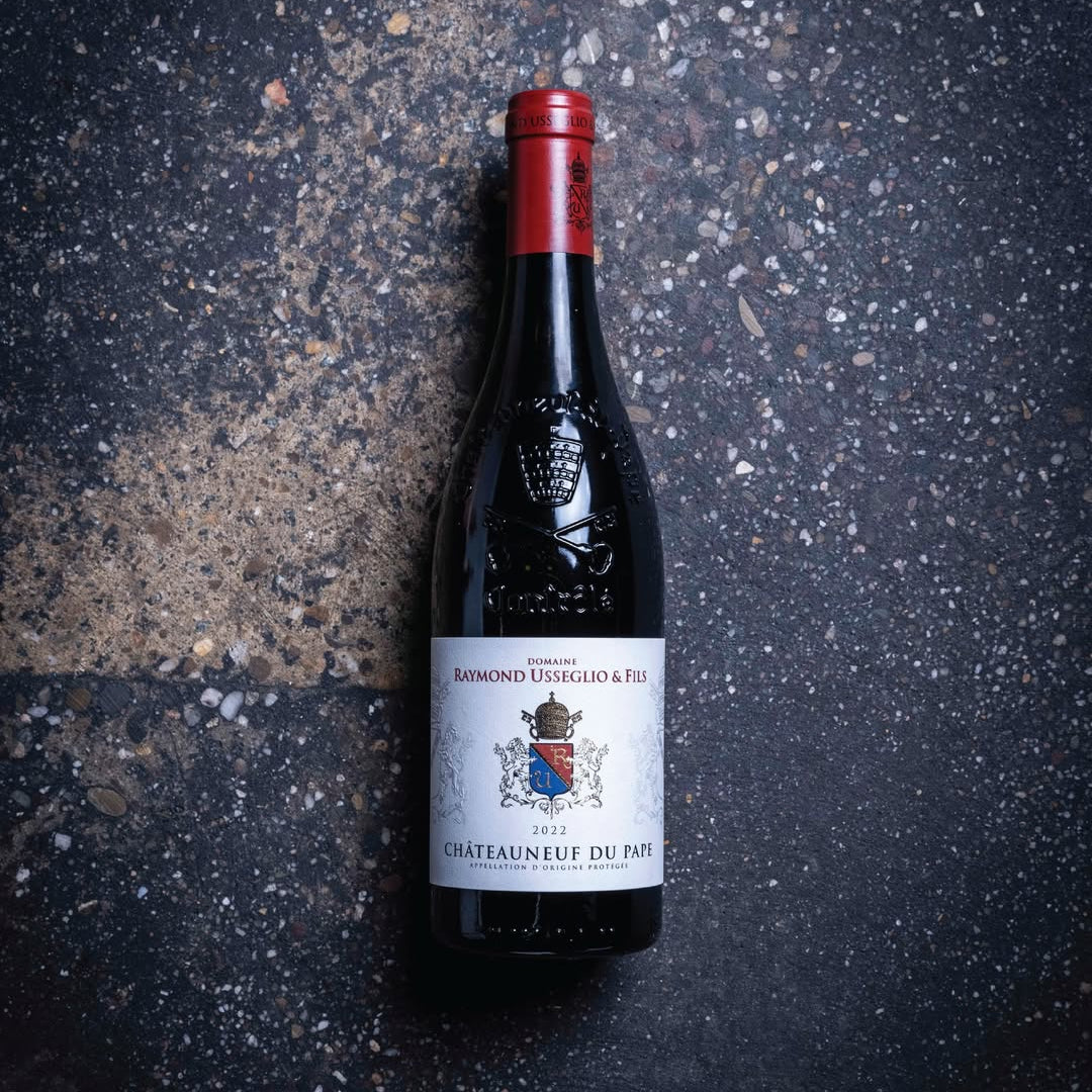 Load image into Gallery viewer, Raymond Usseglio Fils Chateauneuf du Pape wine bottle with a red label on a dark textured surface