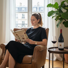 Load image into Gallery viewer, Woman reading a book in a cozy room with a plant and Raymond Usseglio Fils Chateauneuf du Pape wine bottle on a table.