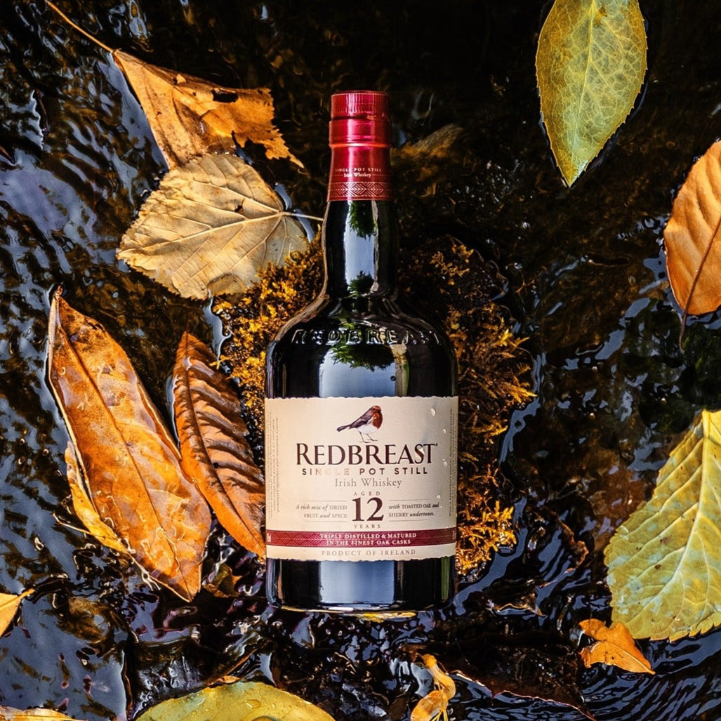 Load image into Gallery viewer, Redbreast 12 year old whiskey bottle surrounded by autumn leaves on a reflective surface
