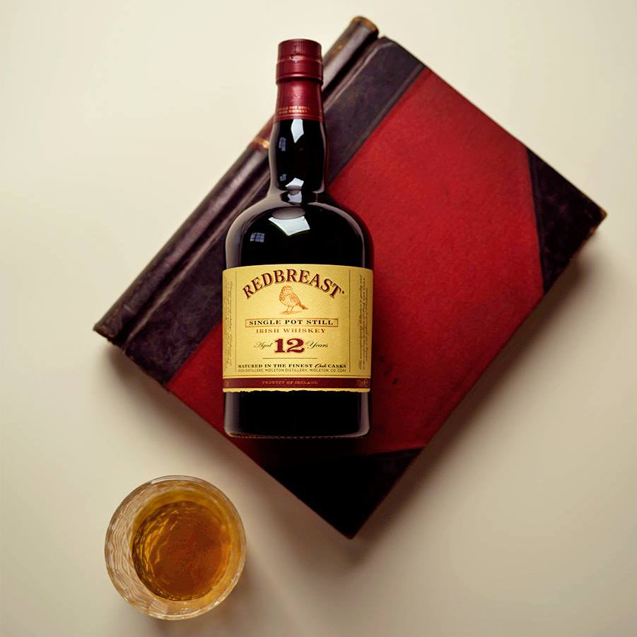 Load image into Gallery viewer, Redbreast 12 year old whiskey bottle with a glass of whiskey on a red and black patterned surface.