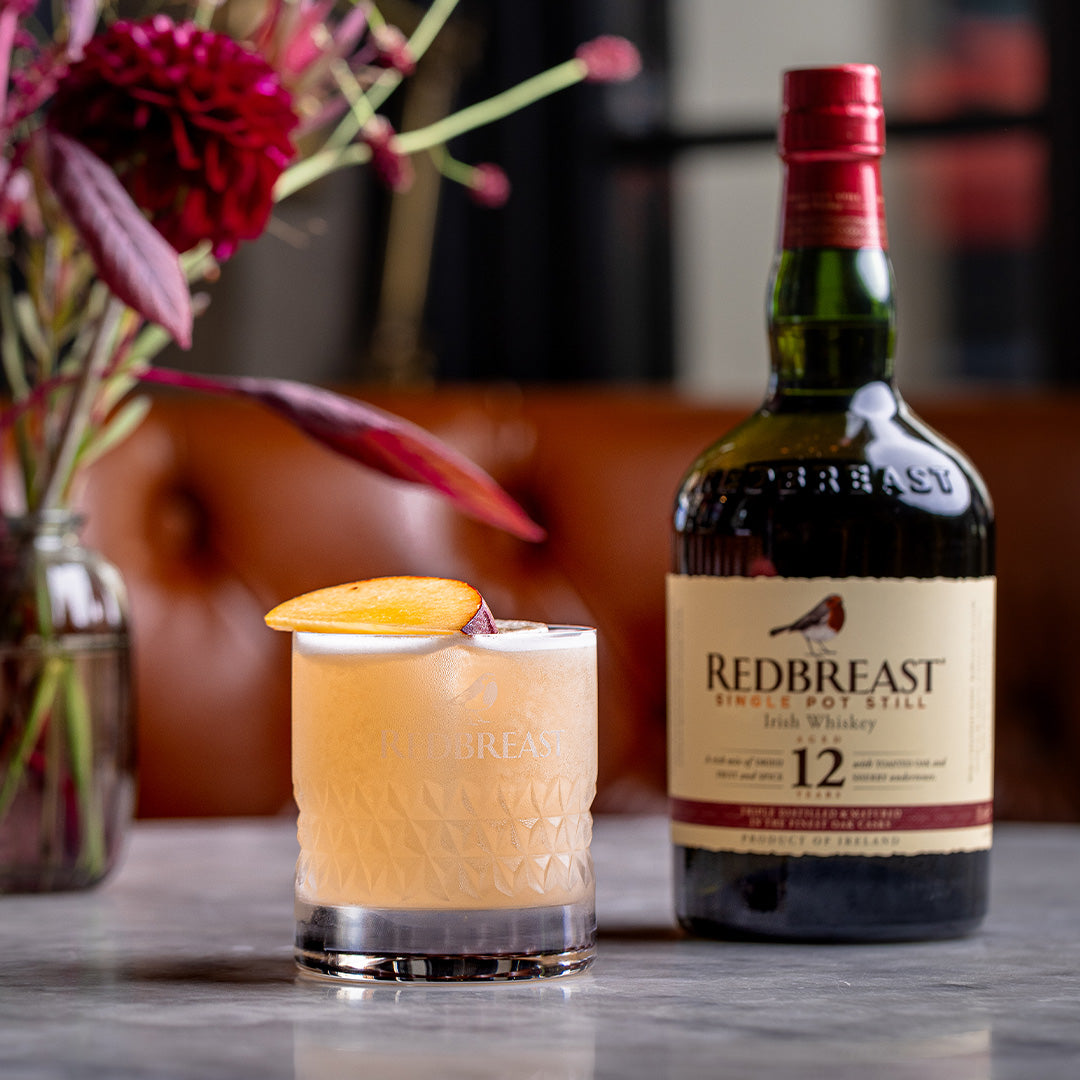 Load image into Gallery viewer, Bottle of Redbreast 12 year old whiskey with a cocktail garnished with an orange peel on a table.