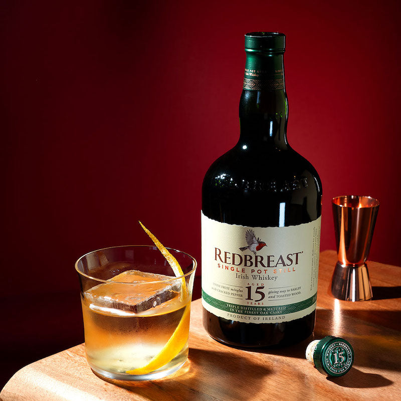 Load image into Gallery viewer, A bottle of Redbreast 15 year old whiskey on a wooden table and a glass full of whiskey on a red background