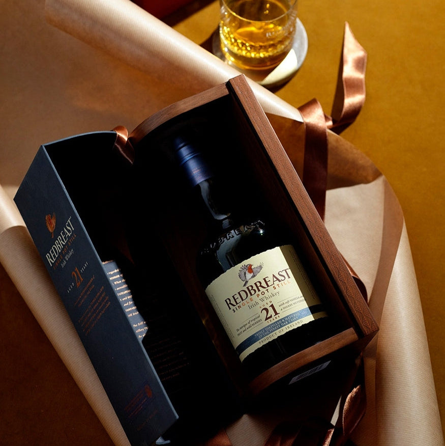 Redbreast 21 year old whiskey bottle in a gift box with a glass of whiskey in the background