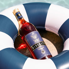 Load image into Gallery viewer, Bottle of Trionfale wine in a blue and white inflatable ring on a sandy surface.
