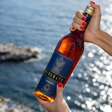 Load image into Gallery viewer, Bottle of Rinomato held by a hand with red nails against a scenic background.