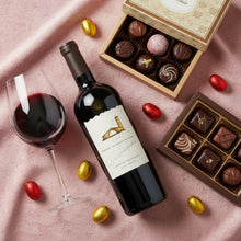 Load image into Gallery viewer, Bottle of Mondavi_Napa Cabernet Sauvignon wine with a glass, chocolate truffles, and candies on a pink surface