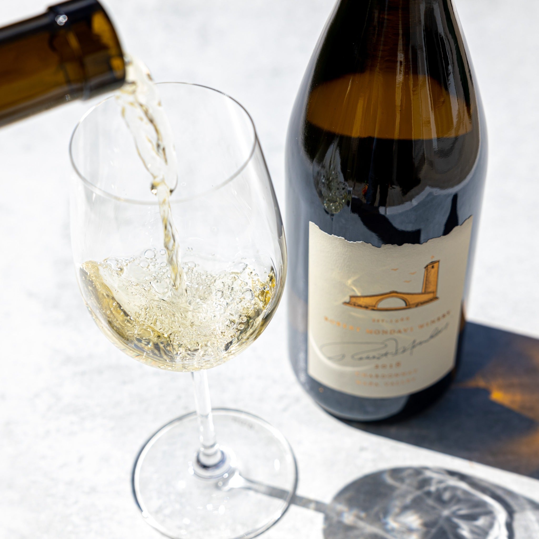 Load image into Gallery viewer, A bottle of Robert Mondavi Napa Chardonnay and someone pouring a glass of wine on a white background