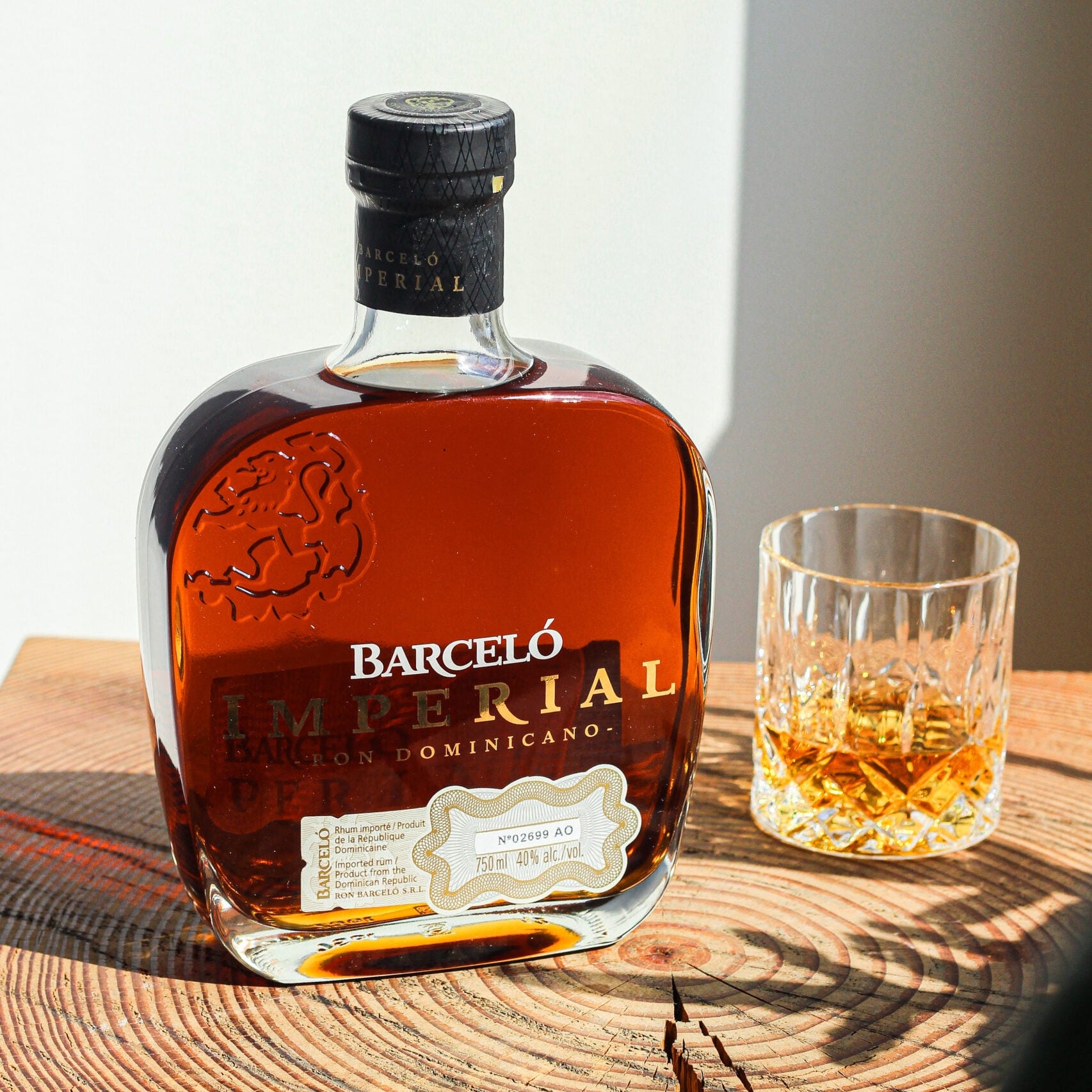Load image into Gallery viewer, A bottle of Barceló Imperial rum with amber liquid and a clear glass tumbler filled with the drink, placed on a rustic wooden surface against a softly lit neutral background.