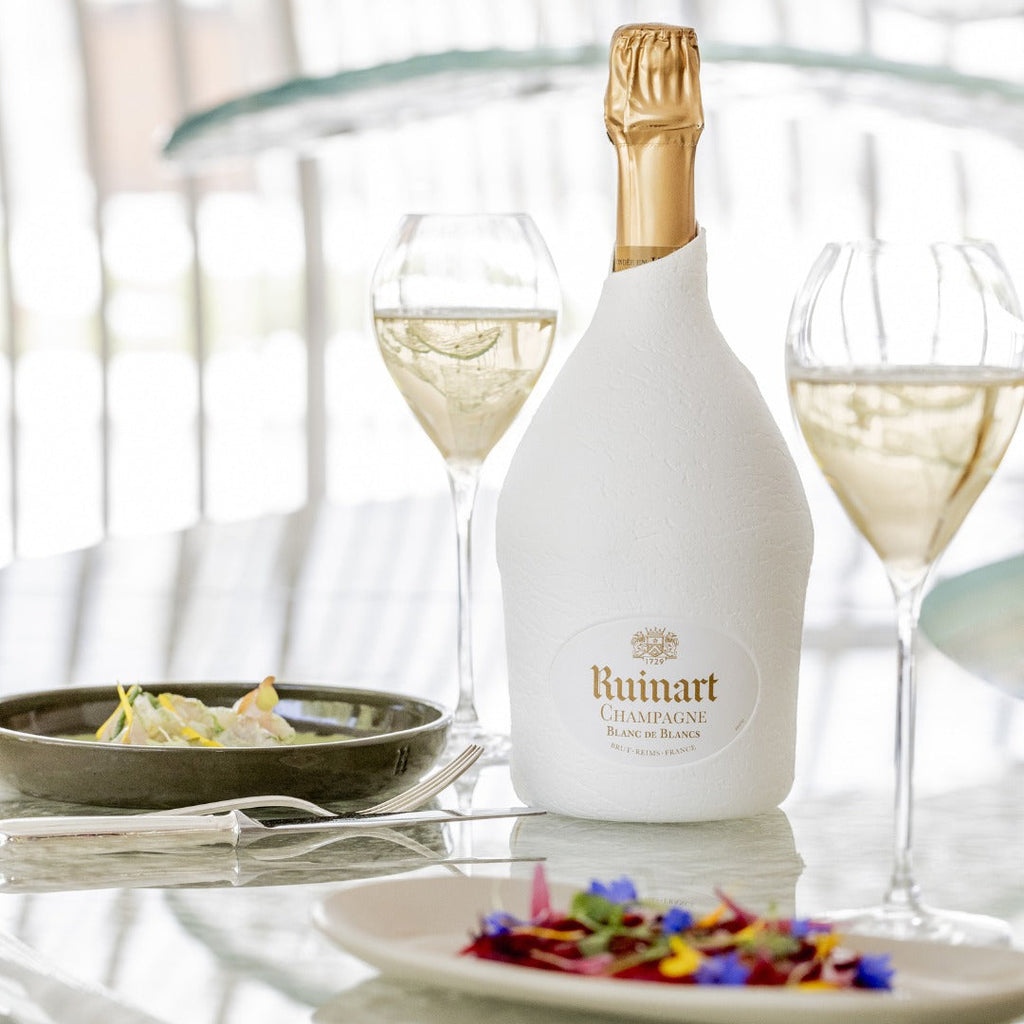 Bottle of Ruinart champagne on a table with two glasses and plates.