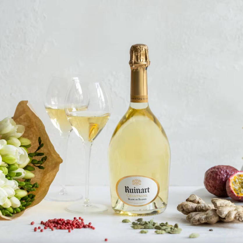 Load image into Gallery viewer, A bottle of champagne and glasses on a white table with some spices and a bouquet of white flowers