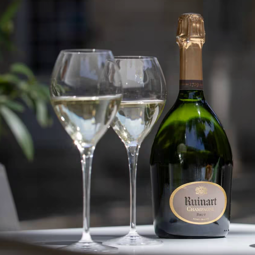 Load image into Gallery viewer, A bottle of Ruinart R de Ruinart Champagne and glasses with a blurry background