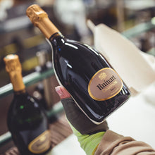Load image into Gallery viewer, Person holding a bottle of Ruinart champagne in a social setting.