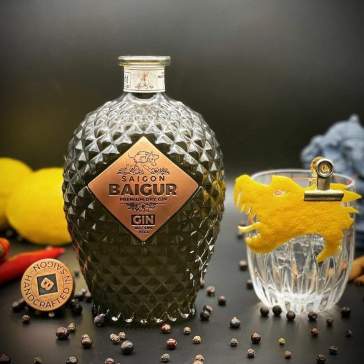 Bottle of Saigon Baigur Gin with a glass and garnishes on a dark surface