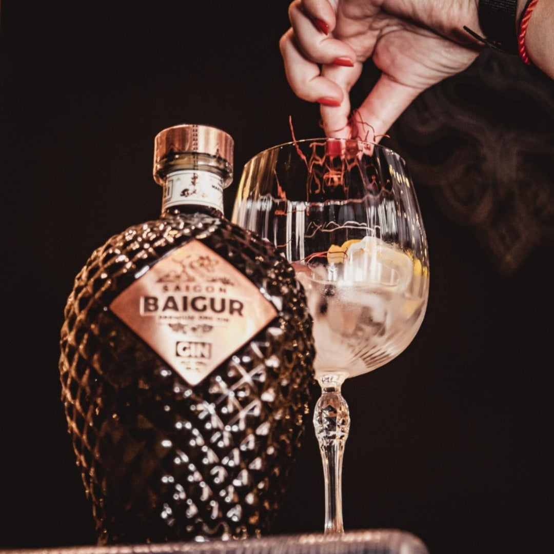 Load image into Gallery viewer, Bottle of Saigon Baigur Vietnamese Premium Dry Gin with a hand pouring into a glass against a dark background